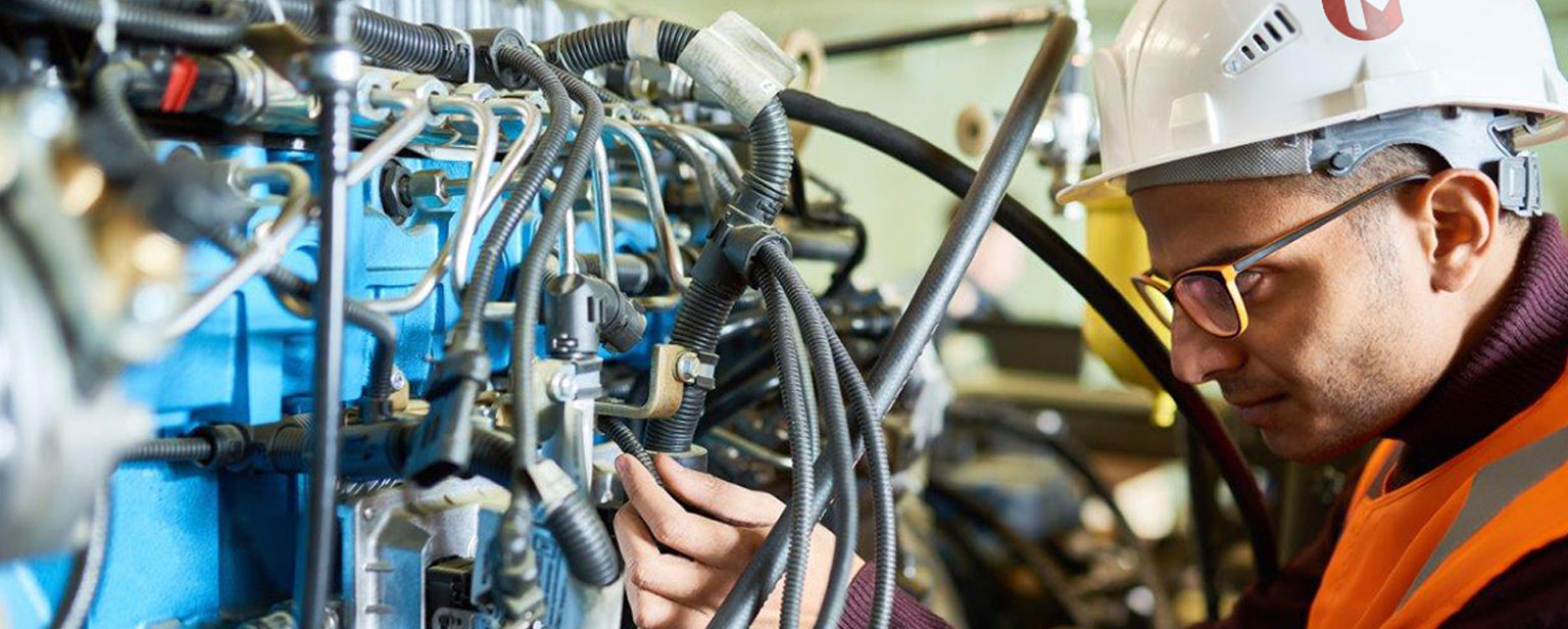 Engineer in a hard hat and safety vest inspecting a complex network of hydraulic and electrical components